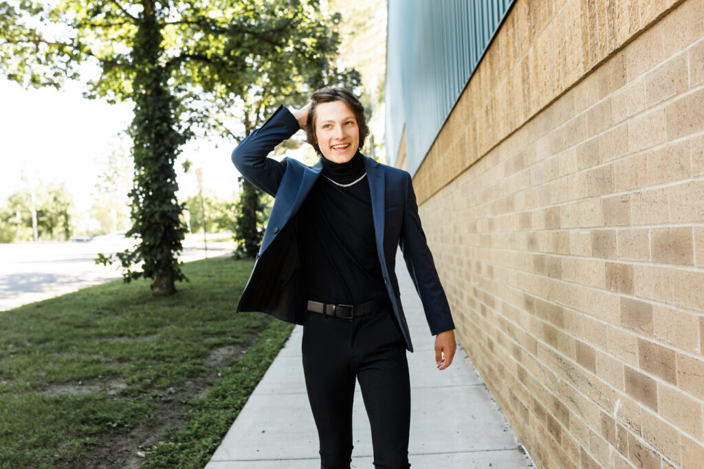 senior boy posing for senior portraits walking in a suit jacket, turtle neck, gold chain and black pants