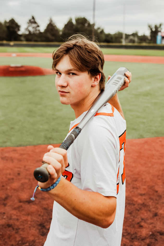 senior boy posing for senior portraits in baseball jersey with bat behind his back