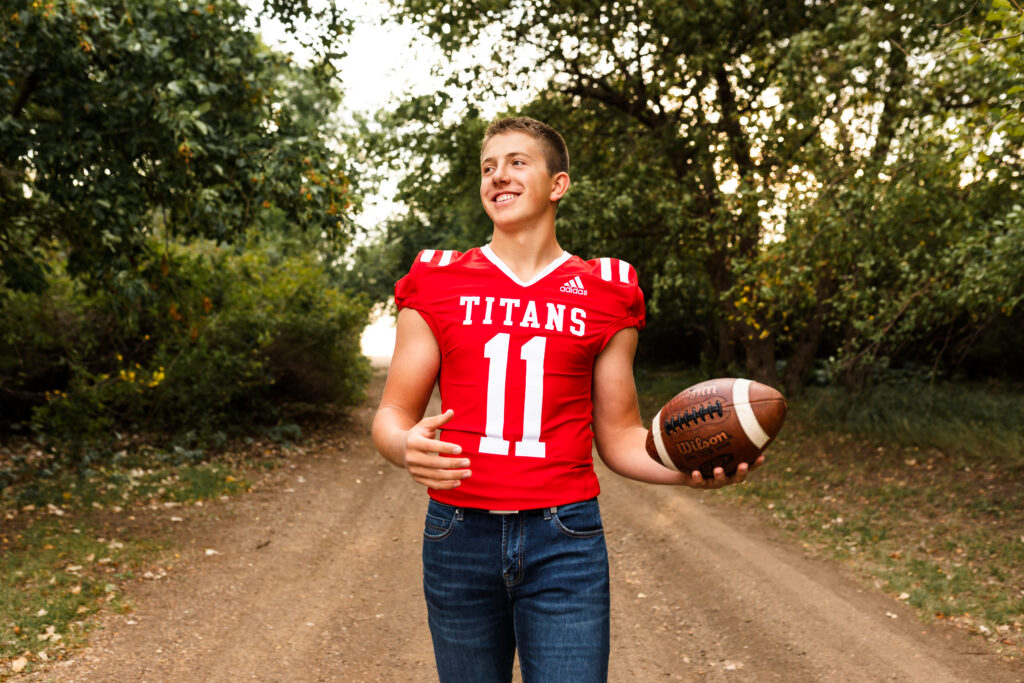 senior boy posing for senior portraits in football jersey and jeans