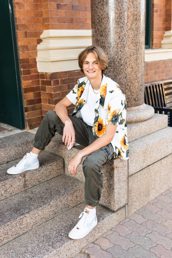 senior boy posing for senior portraits in a floral button down and casual green cargos