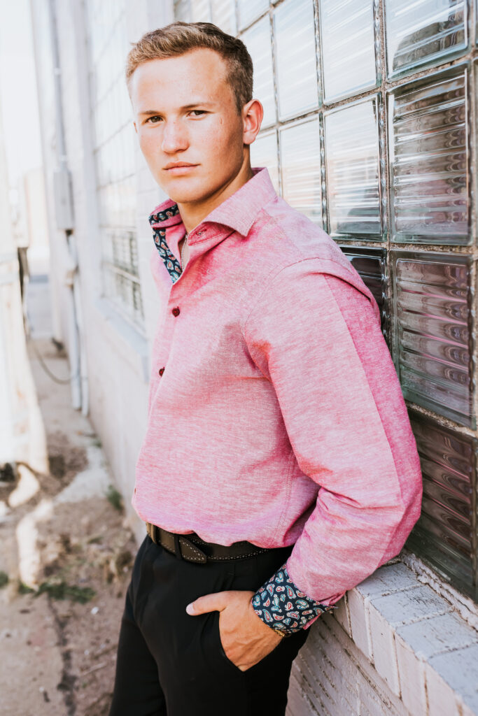 senior boy posing for senior portraits in a nice pink button up shirt 
