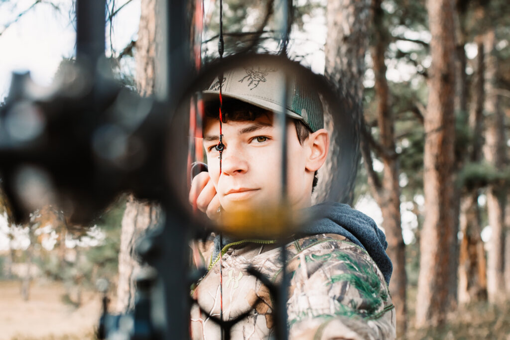 senior boy posing for senior portraits in camouflage holding his bow and looking through it