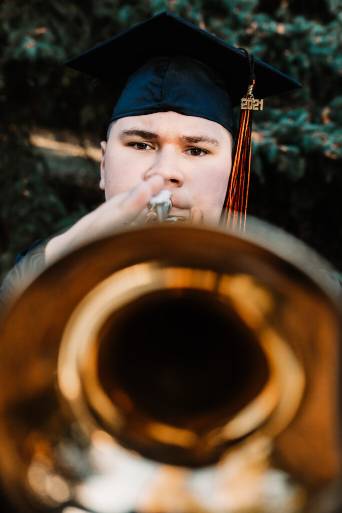 senior boy posing for senior portraits in cap and gown with his trumpet